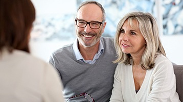 Smiling older couple speaking with an implant dentist in Longmont
