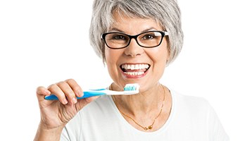 Older woman with dental implants in Longmont holding a toothbrush
