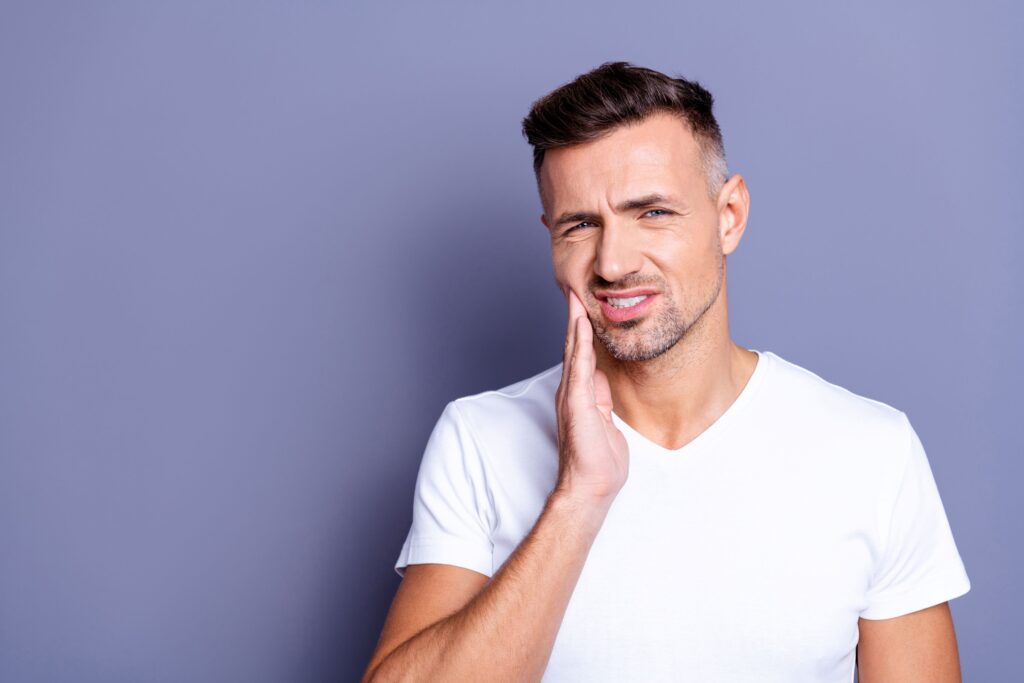 Man pressing hand to jaw in pain with purple background